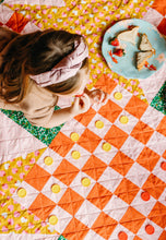 Load image into Gallery viewer, Overhead shot of a pink and red checkerboard quilt. Checkers pieces are placed on the quilt ready to play while a girl sits and eats her picnic lunch, preparing for her move.
